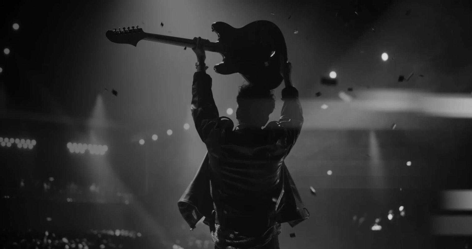 Silhouette einer Person mit hochgehobener E-Gitarre auf einer Bühne vor Publikum